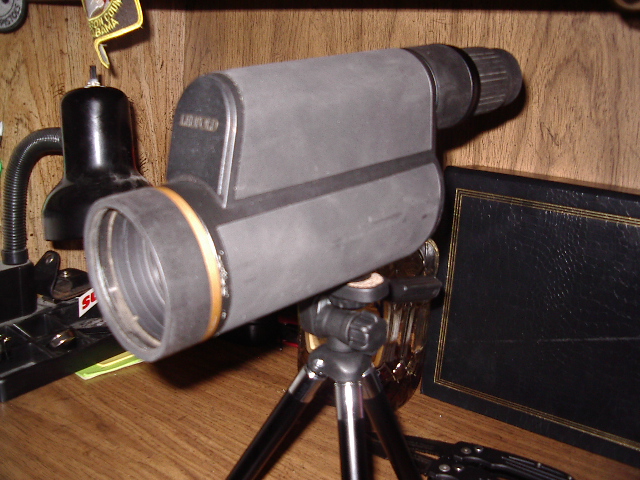 Spotting scope on a small tripod, with a black lamp and a book in the background
