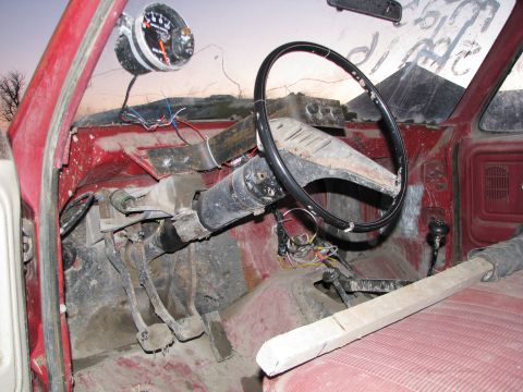 1980 Ford F-250 - The interior of a red 1980 Ford F-250 shows significant wear and tear, with an added gauge on the dashboard.
