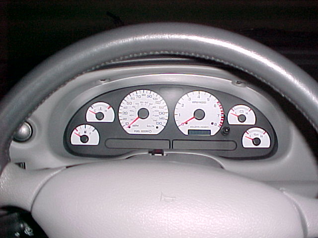 White-face Mustang gauge cluster with red needles seen through gray steering wheel