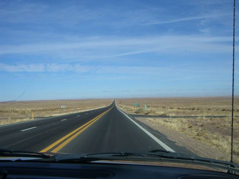 1996 Ford Probe - A long, straight highway cuts through a barren landscape under a vast, partly cloudy sky.