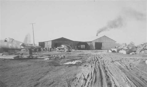 1969 Lincoln Continental - An old airplane and a vintage car are seen at an industrial facility with smoke rising from a building.
