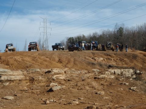 1991 Ford F-150 - A group of off-road vehicles and people are on a dirt hill under a blue sky with power lines.