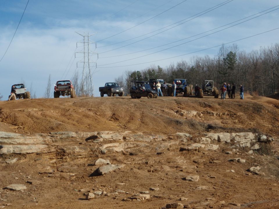 Lifted 4x4 trucks and buggies parked on a clay ridge at an off-road park with spectators