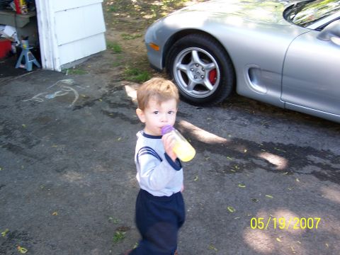 1996 Ford Probe - A young child drinks from a bottle next to a silver sports car in a driveway.