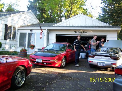 1996 Ford Probe - A red sports car with a black hood is parked in front of a house with an open garage.