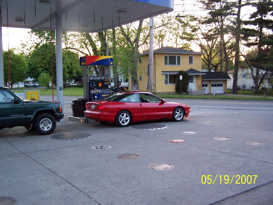 Red 1996 Ford Probe parked at a gas pump next to a green SUV