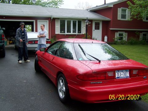1996 Ford Probe - A red coupe with a 'PROBE' badge is parked in front of a house, with two men standing beside it.