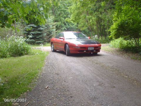 1996 Ford Probe - A red 1996 Ford Probe with a black hood sits on a gravel driveway on a sunny day.