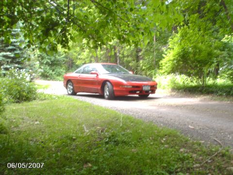 1996 Ford Probe - A red 1993 Ford Probe with a black hood sits on a gravel road surrounded by trees.