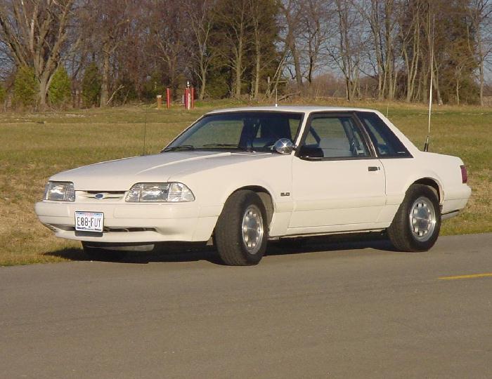White 1993 Ford Mustang coupe parked on asphalt with trees in background