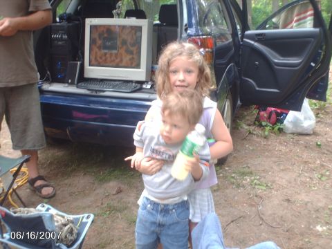 1996 Ford Probe - A computer is set up in the back of a car, with two children posing for a photo.
