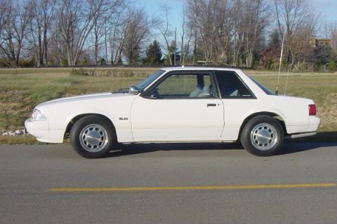 1993 Ford Mustang - A white 1993 Ford Mustang coupe is seen from the side, parked on a road with a yellow line.