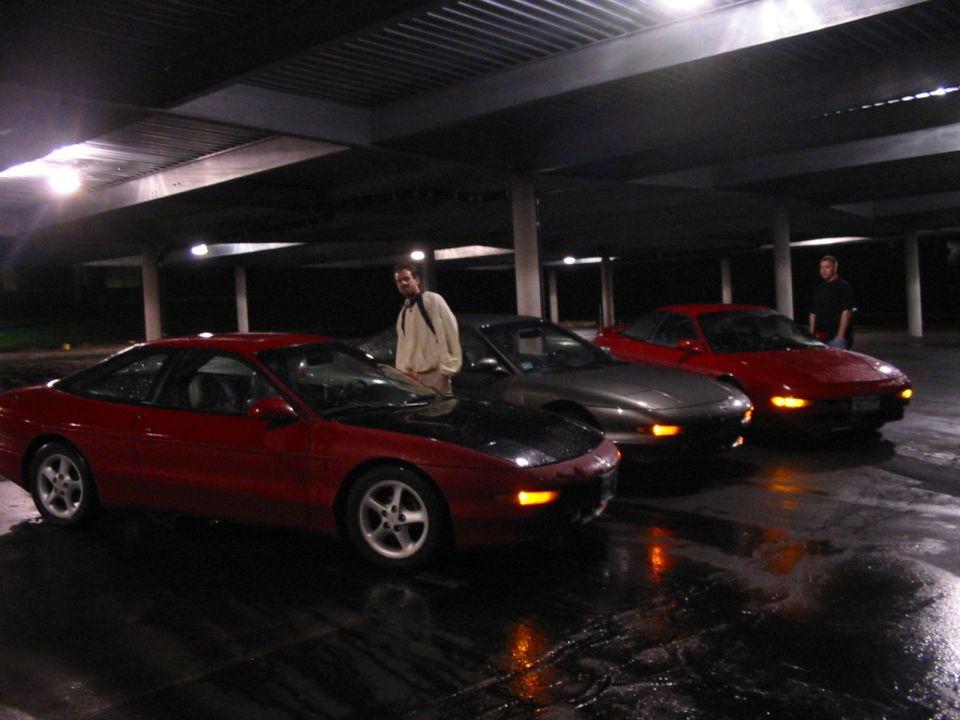 Three red and gray coupes parked in a covered garage. One has a black hood