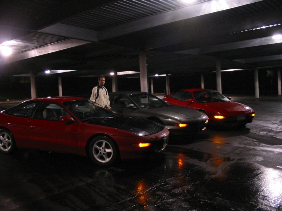 Three red and gray Ford Probes parked in a covered lot at night, wet ground reflects lights