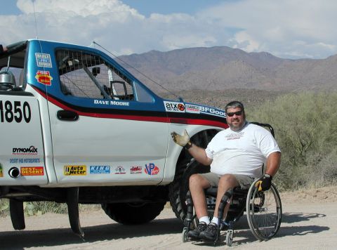 2000 Ford F-150 - A man in a wheelchair poses next to a custom off-road racing truck with sponsor decals.