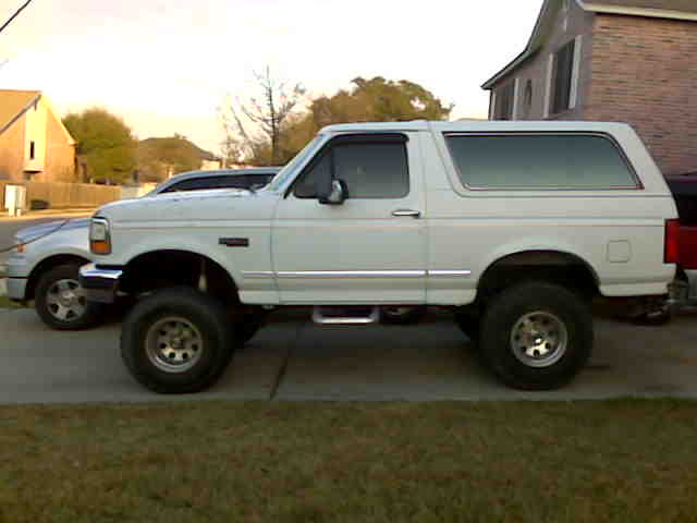 White Ford Bronco with lifted suspension and aftermarket wheels parked next to a silver sedan