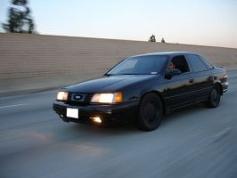 1991 Ford Taurus - A black 1991 Ford Taurus sedan is captured in motion on a highway during the day.