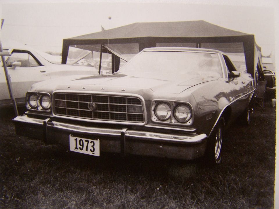 1973 Ford Ranchero front view with a license plate showing '1973'. Another vehicle is partially visible to the left