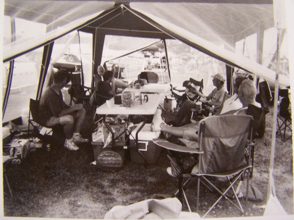 People sitting around a table inside a large tent, with coolers and camping gear visible