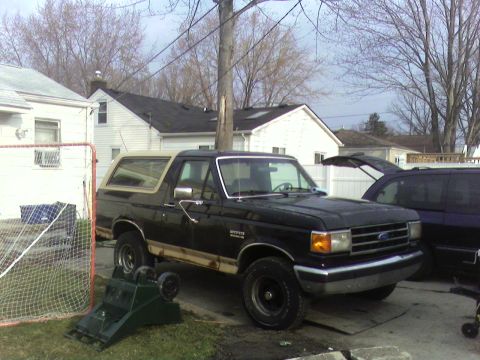 1990 Ford Bronco - This black 1990 Ford Bronco with a tan top is parked in a residential driveway next to another vehicle.