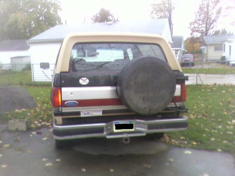 1990 Ford Bronco - Rear view of a 1990 Ford Bronco with a tan removable top and a spare tire on the back.
