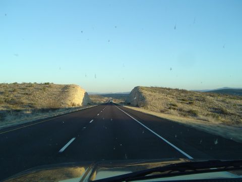 1989 Ford Bronco - A long, straight highway stretches through a barren, rocky terrain under a bright, cloudless sky.