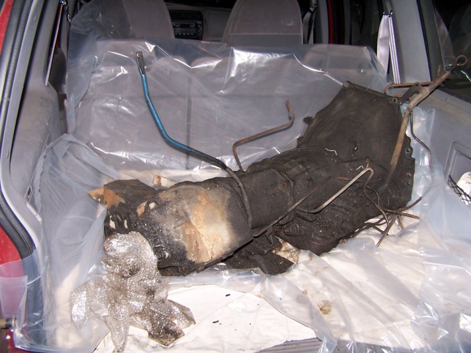 Burnt and corroded transmission and parts laid on plastic in a hatchback cargo area