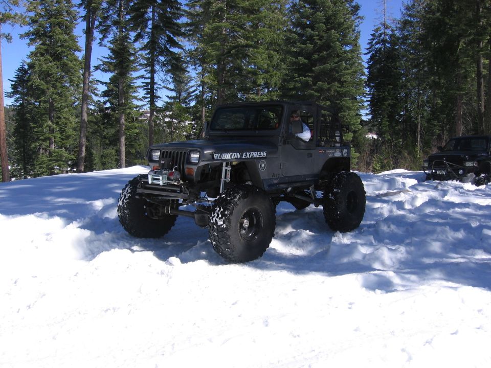 Dark Jeep Wrangler with "Rubicon Express" on door in snow, another vehicle behind