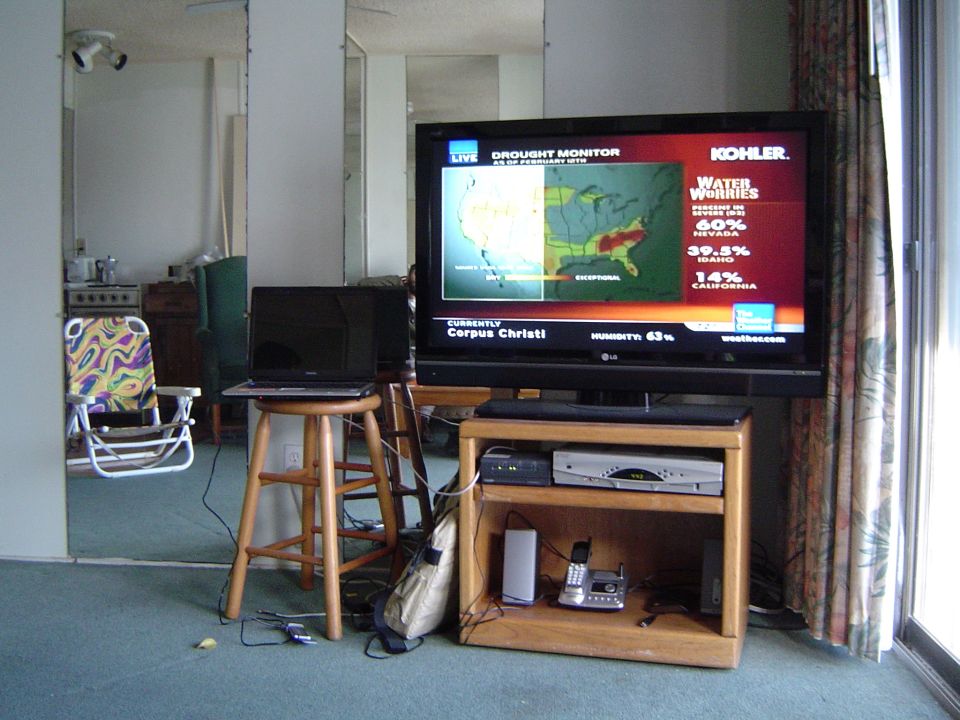 Flat-screen TV on a wooden stand showing a weather news drought map