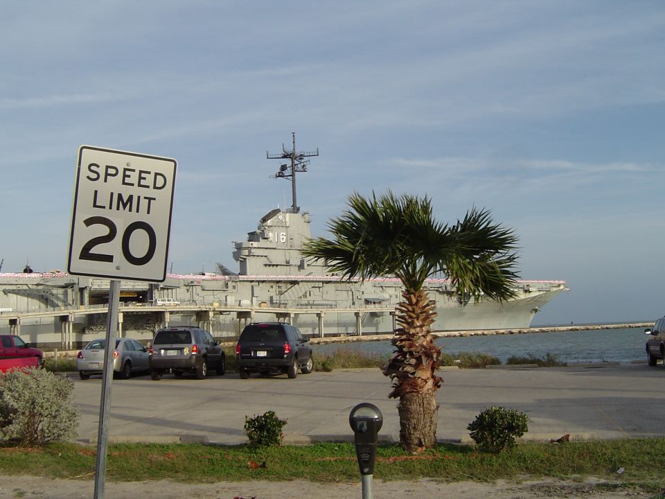 Speed limit 20 sign in front of a parked car and a large ship