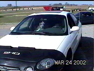 1997 Ford Taurus - A white sedan is partially covered with a black car cover that displays the 'SHO' emblem, with a date stamp of March 24, 2002.