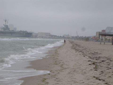 1989 Ford Bronco - A beach scene with an aircraft carrier visible offshore and a person walking along the shore.