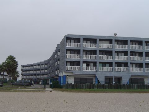 1989 Ford Bronco - A long, gray, multi-story building with many balconies is seen with several vehicles parked in front.