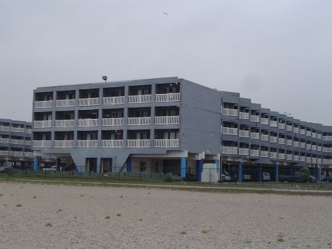 1989 Ford Bronco - Rows of gray hotel buildings stand on stilts along a beach, with a cloudy sky overhead.