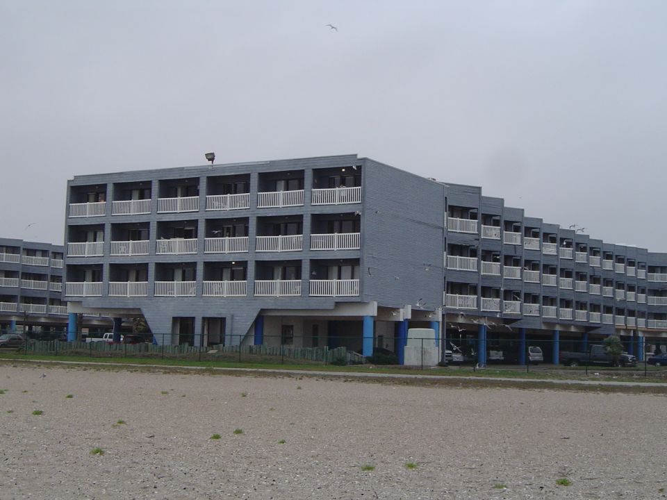 Gray hotel buildings on stilts with white balconies, under a cloudy sky