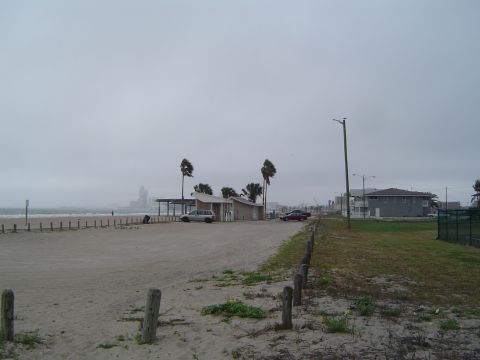 1989 Ford Bronco - Two vehicles are parked on a beach lot under an overcast sky, with buildings and palm trees in the background.