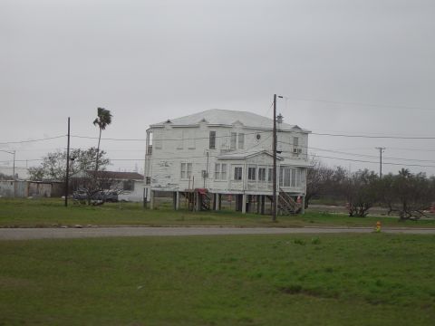 1989 Ford Bronco - A weathered white house stands elevated on stilts, its paint chipped, against a muted sky.