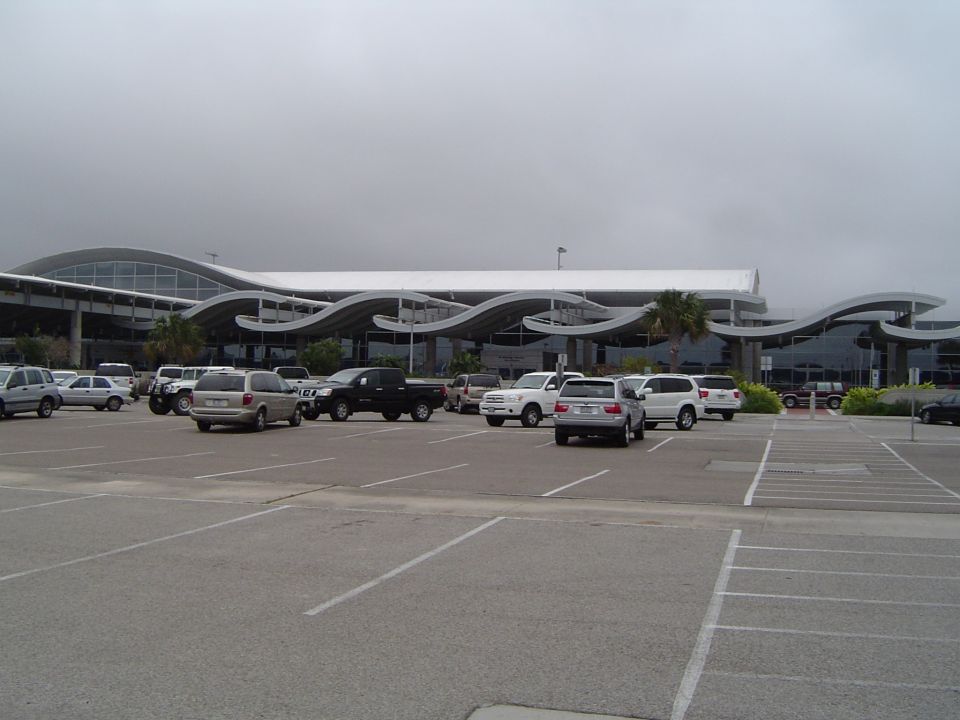 Parking lot in front of a building with wavy rooflines, several cars and trucks parked