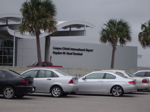 1989 Ford Bronco - The Hayden W. Head Terminal at Corpus Christi International Airport is visible behind several parked vehicles and palm trees.