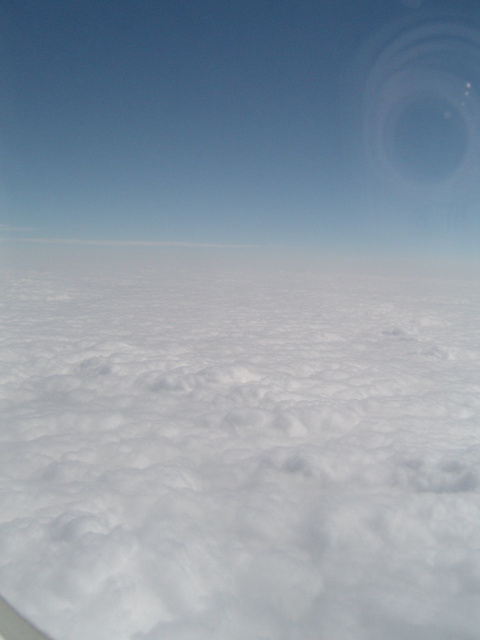 View from airplane window of clouds below and blue sky above