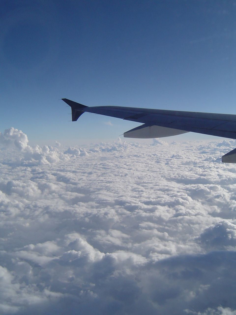 Airplane wing seen from inside the cabin, flying above a thick layer of clouds