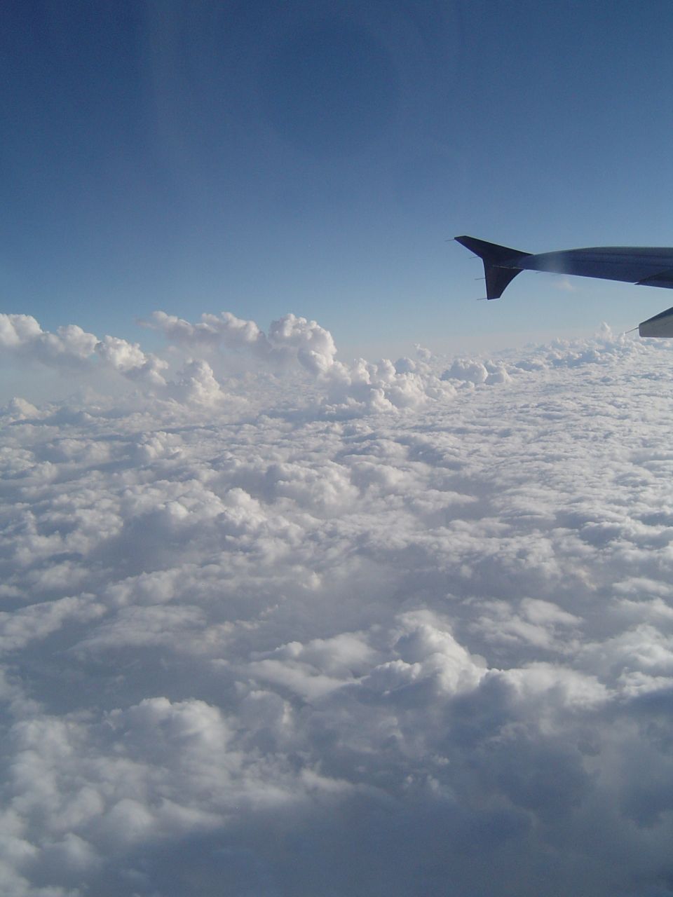 Airplane wing seen from inside the cabin, flying above a thick layer of clouds