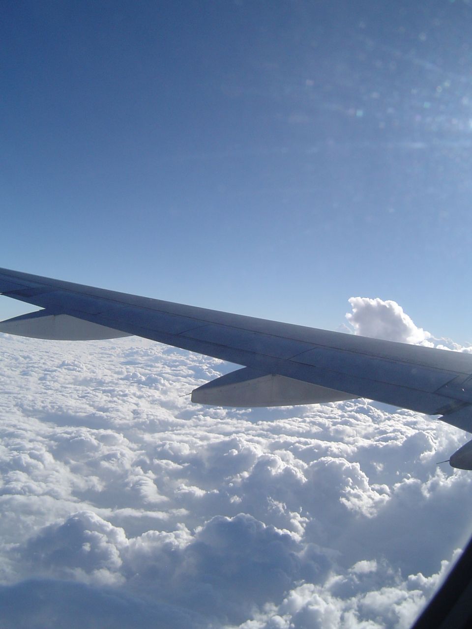 Airplane wing above fluffy white clouds under a clear blue sky