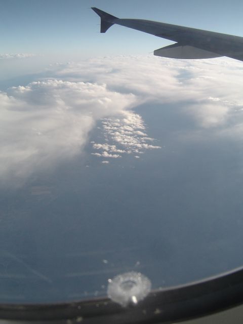 1989 Ford Bronco - Looking out the airplane window at clouds and the wing against a blue sky.