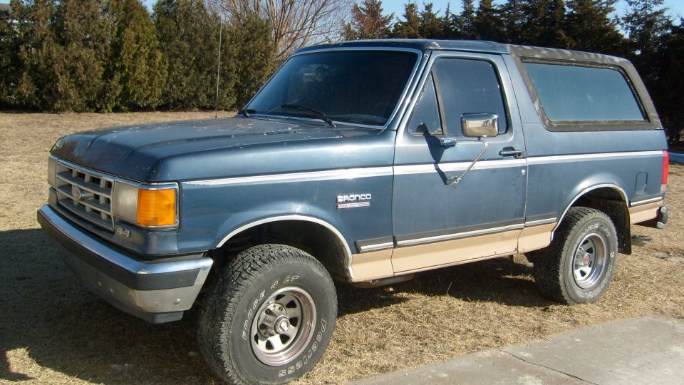 Blue and tan Ford Bronco, front three-quarter driver side view, parked on dry grass