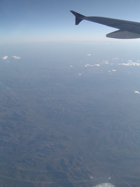1989 Ford Bronco - View from an airplane window shows a wing against a hazy sky and terrain below.
