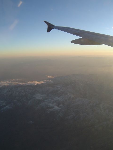 1989 Ford Bronco - View from an airplane window shows a wing against the sky, with mountains and clouds below during sunset.