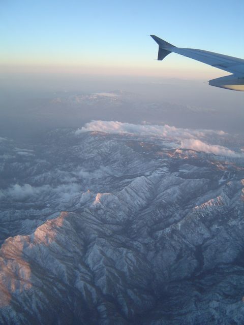 1989 Ford Bronco - View from an airplane window shows an airplane wing above snow-capped mountains during sunrise.