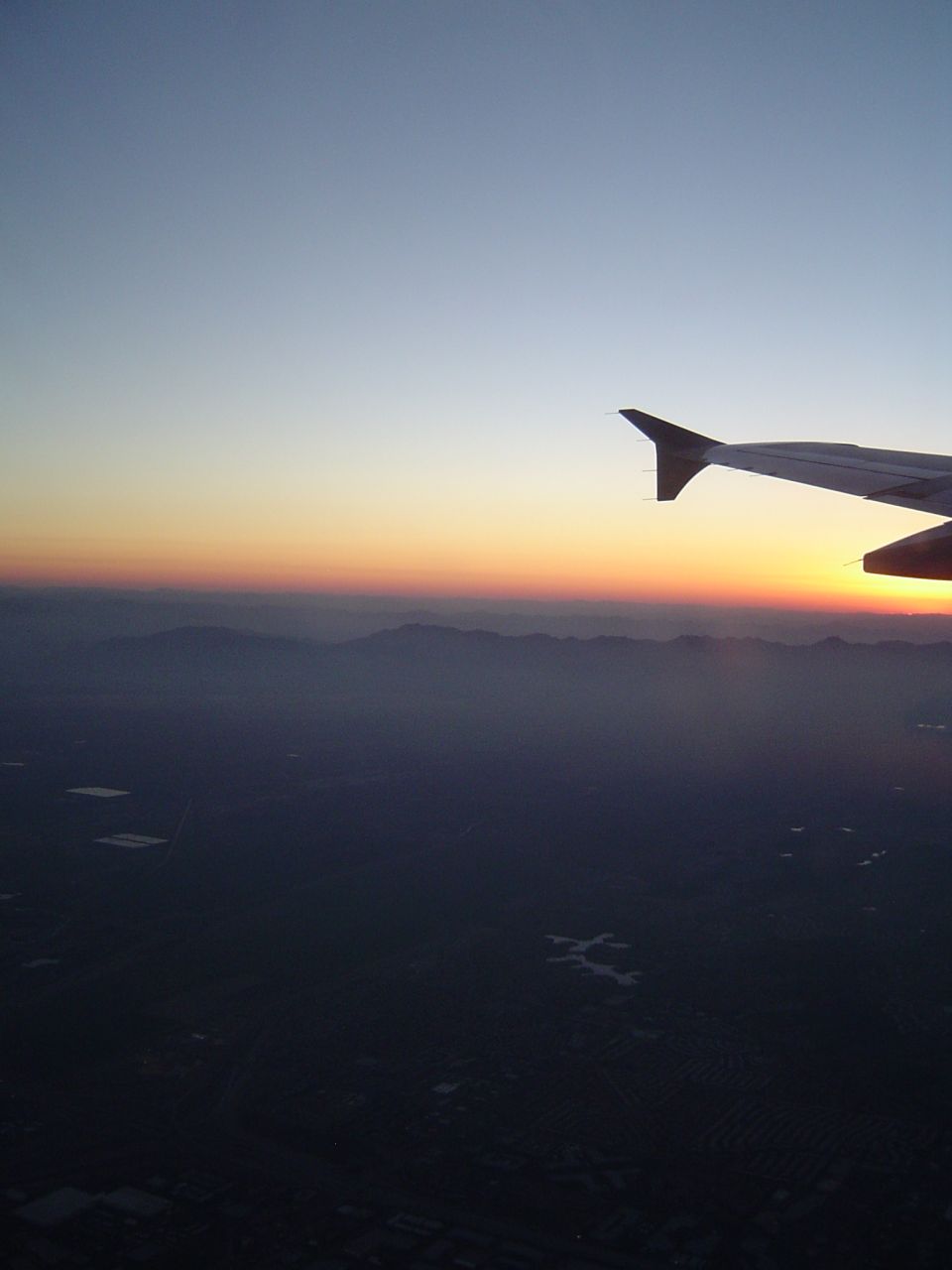 Airplane wing against a sunset sky with mountains and land below