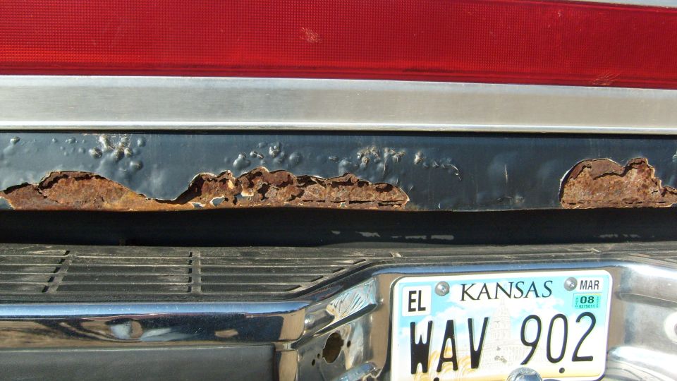 Rust-through along lower tailgate above chrome bumper and Kansas plate WAV 902